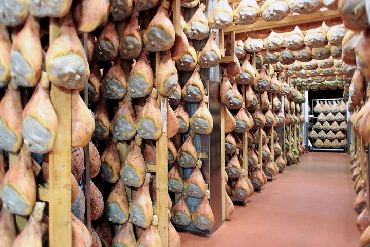 File di prosciutti di Parma appesi a stagionare in una lunga sala